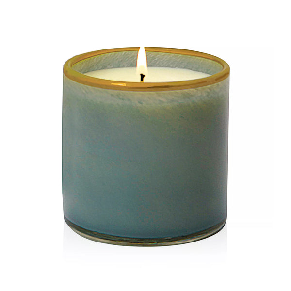 Lafco's Sea & Dune candle is housed in a hand-blown blue glass vessel with a honey-colored rim. The candle's one wick is lit.
