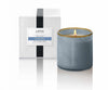 Lafco's Sea & Dune candle sits alongside its signature gift box. The candle is housed in a hand-blown blue glass vessel with a honey-colored rim. The candle's one wick is lit.