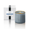 Lafco's Sea & Dune candle sits alongside its signature gift box. The candle is housed in a hand-blown blue glass vessel with a honey-colored rim. The candle's one wick is lit.