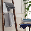 Matouk bath rugs in assorted colors stacked and hanging on a decorative rod.